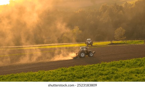 AERIAL, LENS FLARE: Farmers prepare the field for winter rest and planting in spring season. Two tractors ploughing agricultural land on a sunny hillside, with late afternoon sun casting a warm glow. - Powered by Shutterstock