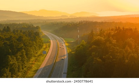 AERIAL, LENS FLARE: Morning light spills over hilly wooded landscape and highway. Trucks and cars travel along the scenic motorway leading through beautiful countryside bathing in golden sunlight. - Powered by Shutterstock