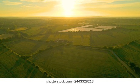 AERIAL, LENS FLARE: View towards the sun rising over scenic English countryside. Beautiful morning light spilling over vast agricultural landscape and green wheat fields on the outskirts of Canterbury - Powered by Shutterstock