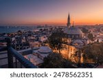 Aerial night cityscape with small residential buildings, illuminated mosque with a minaret and distant lights of ships in the sea, Istanbul, Turkey