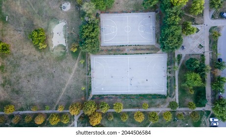 Aerial Outdoor Basketball Court With Players Overhead Shot Top Down View, Daytime. Aerial View Of Street Basketball Court. Kids Are Playing Football In The Field.