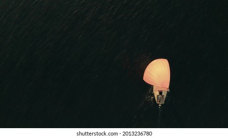 Aerial Overhead View Of An Unknown Sailboat With Orange Sail On The Sea