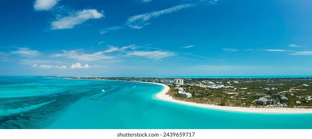 aerial panorama of Grace Bay Beach shows coast of clear white sand lined with lush vegetation, few resorts and clear turquoise water of the Caribbean Sea exposing coral reefs below as boats sail by   - Powered by Shutterstock