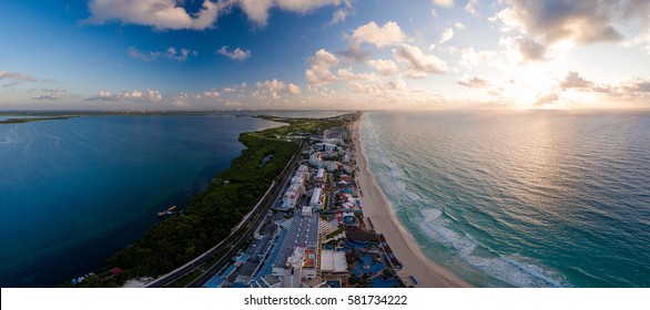 Aerial Panorama Of Hotel Row In Cancun, Mexico Featuring The Major Hotels And Resorts With White Sandy Beaches And Blue Ocean During A Morning Sunrise