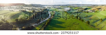 Aerial panorama picture of the river Otter near Honiton and Ottery St Mary. Sunrise and rolling mist cross the lush green fields below. Spectacular landscape. 