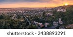 Aerial panorama of residential homes above city of Los Angeles cityscape shot from lush hiking trail in Hollywood Hills at sunset.