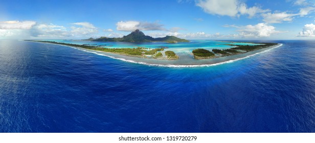 Aerial Panoramic Landscape View Of The Island Of Bora Bora In French Polynesia With The Mont Otemanu Mountain Surrounded By A Turquoise Lagoon, Motu Atolls, Reef Barrier, And The South Pacific Ocean