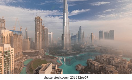 Aerial panoramic view of Dubai city early morning during fog. Sunrise at futuristic city skyline with skyscrapers and towers from above. Sun reflected from glass surface