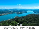 Aerial panoramic view of Lake Wörthersee seen from Pyramindenkogel in Carinthia, Austria. Serene turquoise waters, lush green forests and rolling hills of Austrian Alps. Charming lakeside village