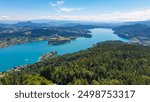 Aerial panoramic view of Lake Wörthersee seen from Pyramindenkogel in Carinthia, Austria. Serene turquoise waters, lush green forests and rolling hills of Austrian Alps. Charming lakeside village