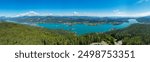 Aerial panoramic view of Lake Wörthersee seen from Pyramindenkogel in Carinthia, Austria. Serene turquoise waters, lush green forests and rolling hills of Austrian Alps. Charming lakeside village