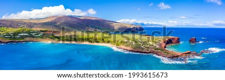 Aerial panoramic view of Lanai, Hawaii featuring Hulopo'e Bay and beach, Sweetheart Rock (Pu'u Pehe), Shark's Bay, and the mountains of Maui in the background.