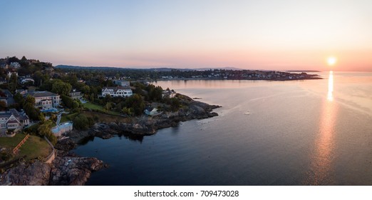 Aerial panoramic view of the luxury homes on top of rocky shore with a beautiful Pacific Ocean scene. Taken in the capital city of Victoria, Vancouver Island, British Columbia, Canada, during sunrise.