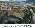 Aerial panoramic view of medieval Elda castle above the town with partially restored walls, towers and gate made of white lime stone in Spain