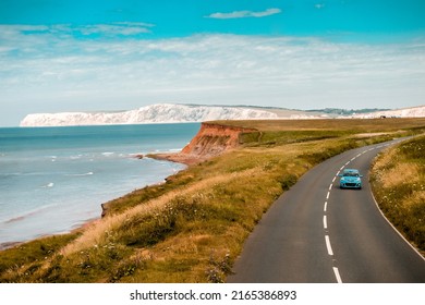 Aerial panoramic view of road with blue car on it with the Needles and sea view. The Isle of WIght, UK