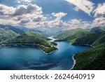 Aerial panoramic view of Vacha Reservoir in Bulgaria, surrounded by lush green hills and forests. Captured by drone in the heart of the Rhodope Mountains.
