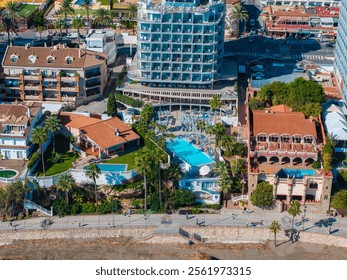 Aerial perspective of Benalmadena, Spain, highlighting a circular hotel, palm trees, a large pool, and traditional buildings with terracotta roofs. - Powered by Shutterstock