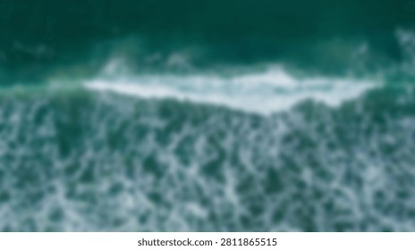 An aerial perspective captures the dynamic motion of ocean waves breaking on the shore, creating white foam and swirling patterns in the clear turquoise water.