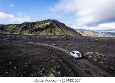 Aerial perspective of a car navigating a sparse basalt road Landmannalaugar in Iceland, surrounded by barren landscapes and bathed in warm sunlight