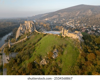 Aerial perspective of Devín Castle in Slovakia. The historic fortress sits atop a rocky hill, with a scenic view of the surrounding landscape and Danube River on sunset. - Powered by Shutterstock