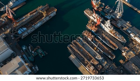 Aerial perspective of a crowded shipyard with multiple dry docks occupied by large ships undergoing maintenance and painting supported by heavy industrial cranes