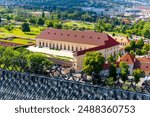 Aerial perspective of the historical Prague Castle Riding Hall with its red roof, captured on a sunny summer day, surrounded by lush green gardens. Prague, Czechia