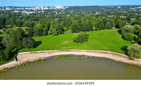 An aerial perspective recedes from two boys playing soccer in an open field within a picturesque park on a sunny day, transitioning to a wide-ranging view of the surrounding area with the city skyline - Powered by Shutterstock