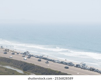 Aerial perspective of San Diego's coastal area, featuring a road parallel to the beach, parked cars, beachgoers, and the Pacific Ocean under clear skies. - Powered by Shutterstock