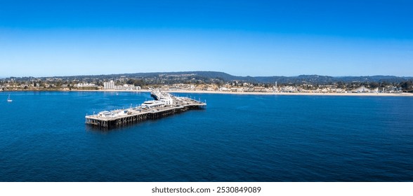 Aerial perspective of Santa Cruz, California, featuring the Santa Cruz Wharf, Beach Boardwalk, and lush greenery against a clear sky and calm sea. - Powered by Shutterstock