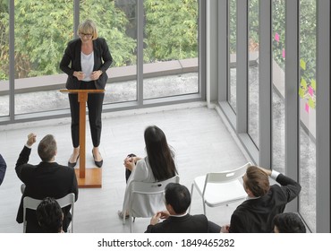 Aerial Perspective View Of Business People In Corporate Seminar Event Meeting In Small Group. Senior Woman Stand Making A Speech To The Audience At The Office Conference Room.