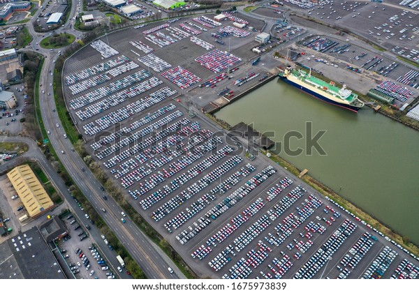 Aerial photo of a car storage yard in the town of\
Grimsby in the UK, The Vehicle Delivery Service yard is located on\
the Humber river showing hundreds or brand new cars being waited to\
board a boat.