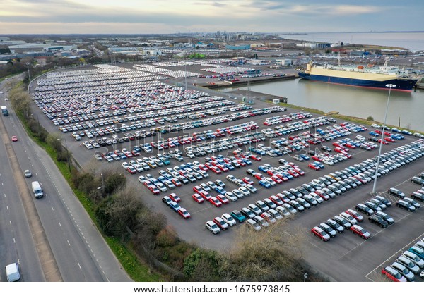 Aerial photo of a car storage yard in the town of\
Grimsby in the UK, The Vehicle Delivery Service yard is located on\
the Humber river showing hundreds or brand new cars being waited to\
board a boat.