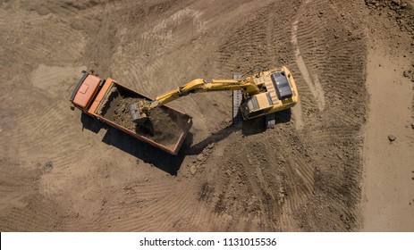Aerial photo of excavator pours sand into the truck. On the construction site top view. Shooting from the drone.