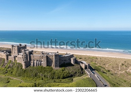 Aerial photo of the famous Bamburgh Castle, a castle on the northeast coast of England, by the village of Bamburgh in Northumberland showing a drone view of the castle and sandy beach in the summer.
