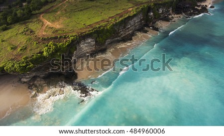Aerial photo from flying drone of an amazing nature scenery with rock cliff on sandy coastline. Beautiful sea water with waves for surfing in summer season in Bali. Beauty Indian ocean landscape