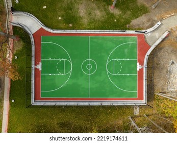 Aerial photo of a green and red outdoor basketball court at school playground.  Court includes retaining walls and black vinyl coated chain link fence.	