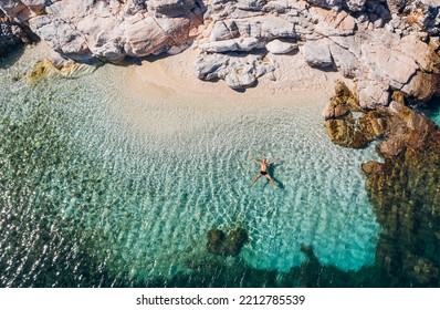 Aerial photo of man lying on the water in STAR pose on rocky pebbly beach and sun tanning. Soft waves washing his body on lonely deserted Greek island in Ionian Sea . Exotic vacation concept - Powered by Shutterstock