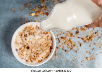 Aerial Photo With Selective Focus On A Person Pouring Almond And Coconut Milk Into A Bowl Full Of Granola On A Light Blue Wooden Surface