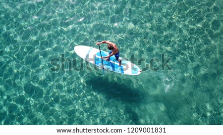 Aerial photo of unidentified man practicing stand up paddle board or SUP in tropical exotic turquoise calm sea sandy beach