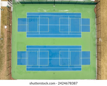 Aerial photo of unusually painted outdoor blue tennis courts with yellow pickleball lines and green out of bounds area.	
