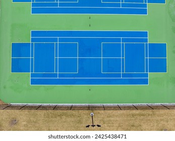 Aerial photo of unusually painted outdoor blue tennis courts with yellow pickleball lines and green out of bounds area.	