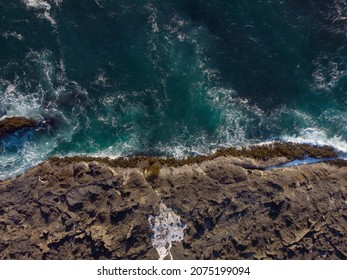 Aerial photograph. Beautiful seascape. Dark turquoise water with white foamy waves and rocky shore. Minimalism. Abstraction. Beauty of nature. Tourism, travel, ecology.