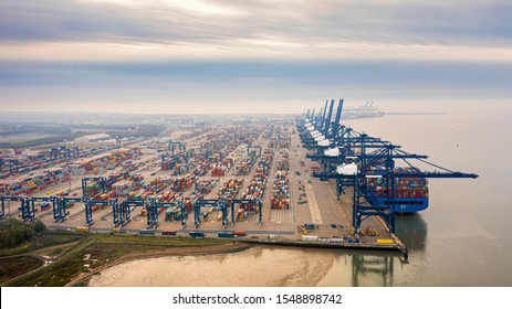 Aerial photograph of Felixstowe container port, rows of stacked multicoloured shipping containers and blue loading gantries converging into the distance viewed hazily through the early morning mist. - Shutterstock ID 1548898742