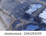 An aerial photograph taken from a helicopter of a capped landfill site in the UK. Snow on black plastic covering an old land fill site. Gas collection pipes.
