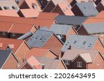 An aerial photograph taken from a helicopter of the roofs of a new build housing estate in the UK. An abstract view of red and grey tiled roofs in a large housing development.