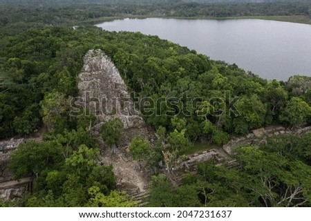 Aerial photography of Coba maya pyramid hidden in the jungle with great lake behind.