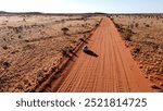 Aerial picture of a car driving in the middle of the outback. Long sandy road with bushes on the side. 4x4 adventure in the red centre of Australia. Northen Territory