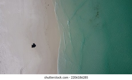 Aerial Picture. Car Parked On The Beach. View From The Sky, Shallow Clear Water And White Sand. 4x4 Off-road And Driving On The Beach. Adventure In Western Australia.