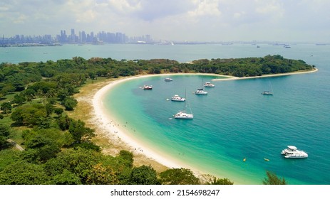 Aerial Picture Of Lazarus Island In Singapore. View To The Beach. Sunny Warm Day. Turquoise Water And Green Forest. Boats Anchored In Shore Water. The Center Of Singapore Is Visible On The Horizon.