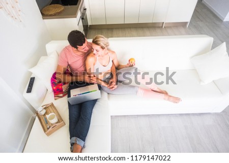 aerial point of view from above for caucasian nice couple in love sitting on the sofa at home and using a laptop together working or wathing a movie. happy modern healthy lifestyle millennial people